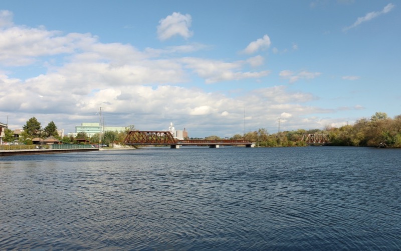 Little Lake in Peterborough with a railway bridge in the distance under a blue sky